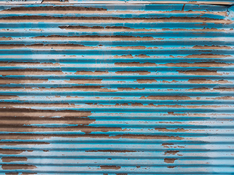 Peeled paint of rolling steel door in blue color. Blue shutter background. Retro style.