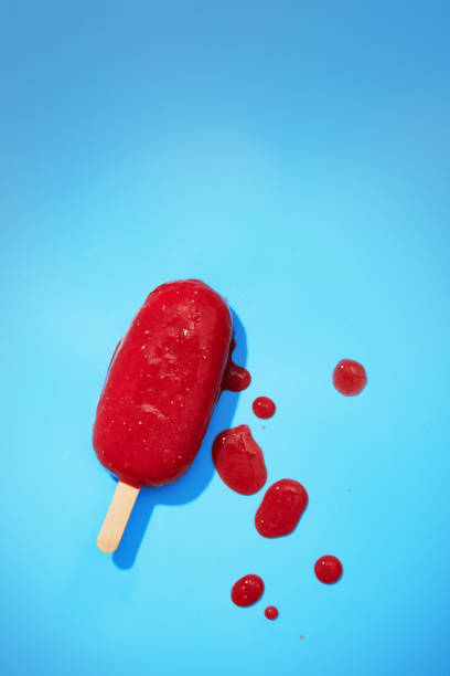 istock Melting red fruit ice cream on a blue background. Colorful summer ice cream on a stick viewed from above. Top view 1136653877