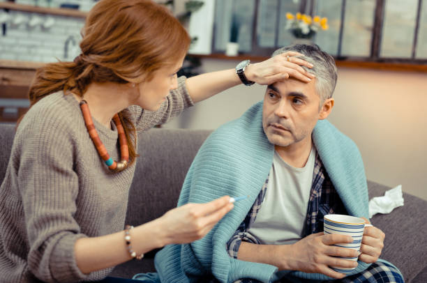 Nice caring woman touching her husbands forehead Measuring the temperature. Nice caring woman touching her husbands forehead while sitting near him cold and flu man stock pictures, royalty-free photos & images