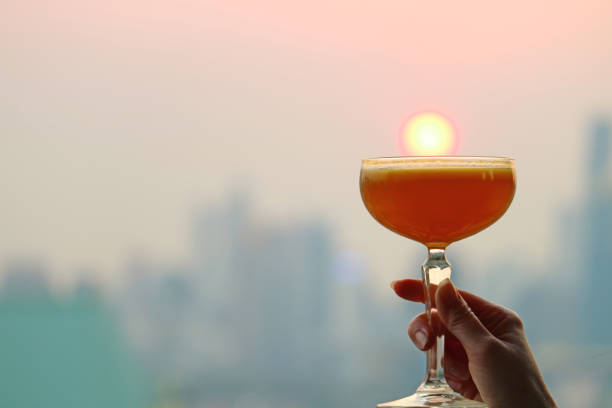 istock Female's hand holding a cocktail glass against setting sun with blurry skyscrapers in backdrop 1136655346