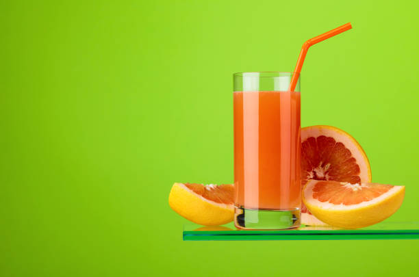 Glass of fresh grapefruit juice with fresh fruits on a green background. Copy space.
