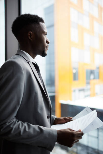 istock Thoughtful young man with papers looking in window 1136659056