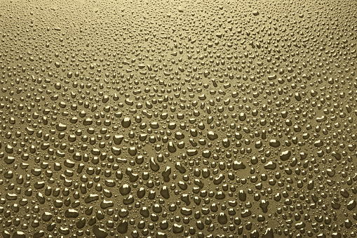 Close-up of water drops on surface, gold background
