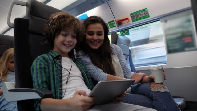 Loving mother watching her son play with digital tablet having fun while commuting on train