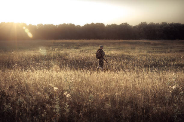 Photo of Hunter men hunting in rural field nearby forest at sunset during hunting season