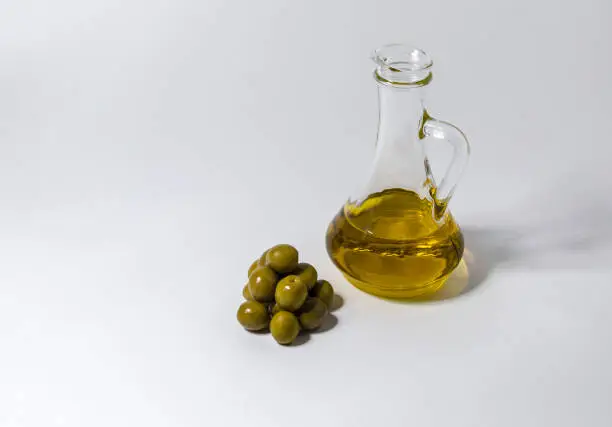 A small jug with oil and some olives on a white background-image