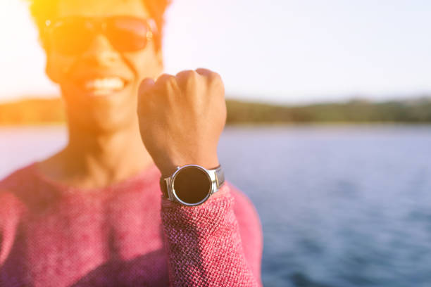 Closeup of happy ethnic guy showing stylish wrist watch with empty dial in bright sunlight