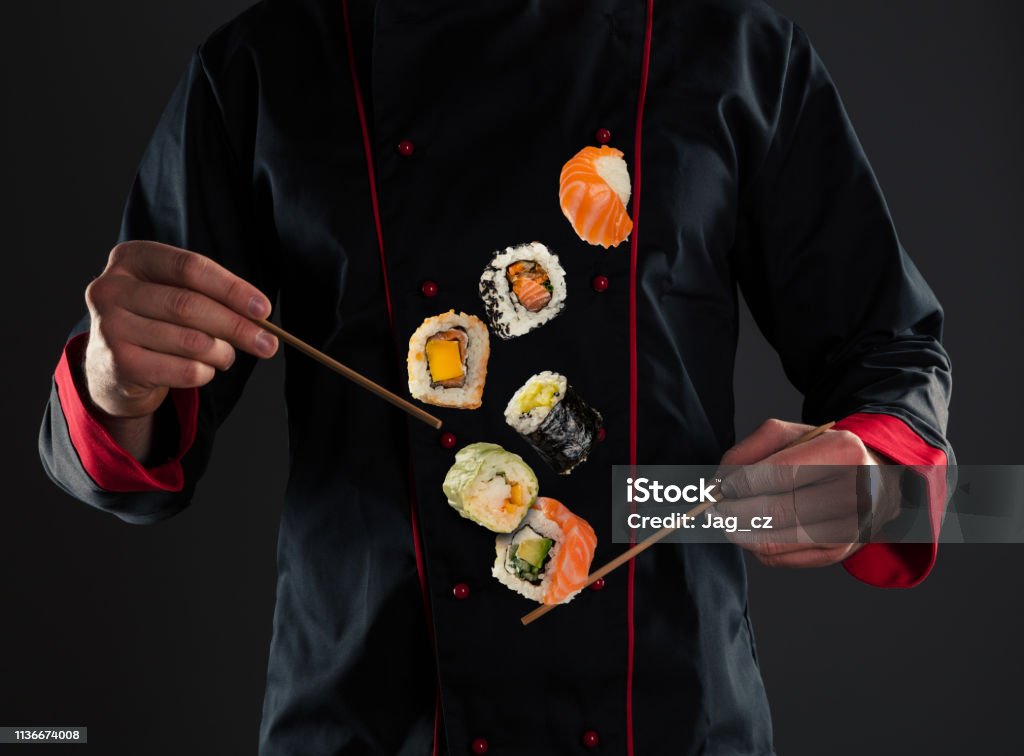 Master chef holding chopsticks with flying sushi Closeup of master chef holding wooden chopsticks with flying sushi pieces. Concept of food preparation, ready for product placement. Chef Stock Photo