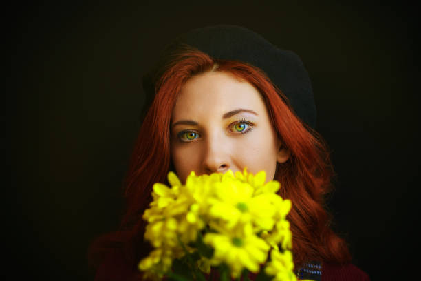 A girl with blue eyes lies on the grass with a bouquet of wildflowers in her hands.