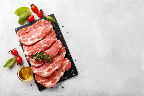 Slices pork loin with spices, olive oil, basil and tomatoes on grey stone background copy space