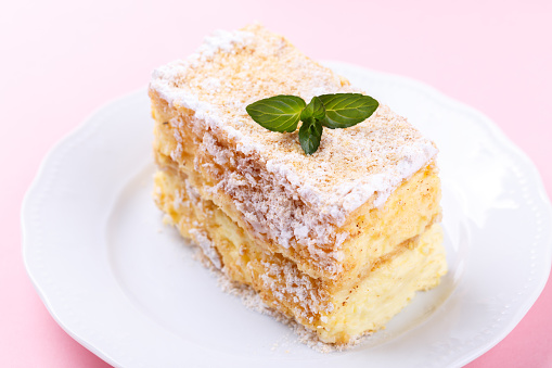 French Mille feuille cake with vanilla cream decorated with mint on a pink background