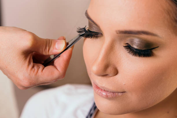 Make up artist placing artificial eyelashes Make up artist working in a make up studio, putting artificial eyelashes on female client's eyelids with a tweezers false lashes stock pictures, royalty-free photos & images