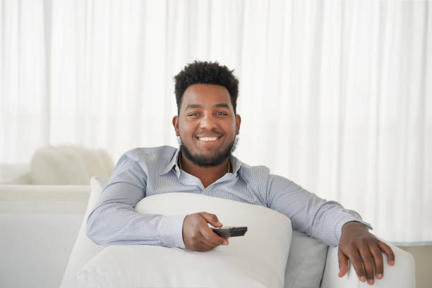 istock young handsome and attractive black african american man sitting at home sofa couch watching television using tv remote controller 1136681672