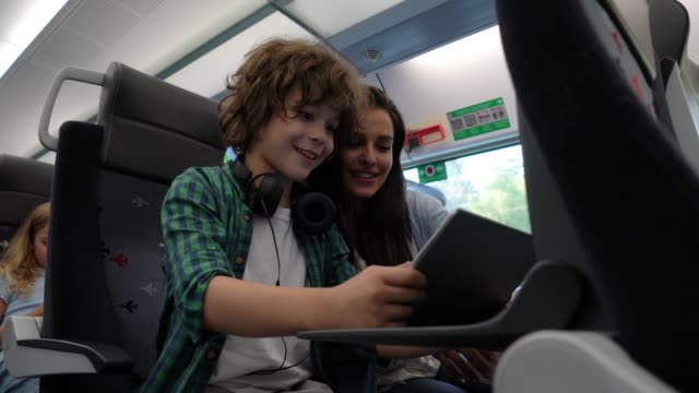 Young mother playing with her son using a tablet talking and laughing while commuting on train