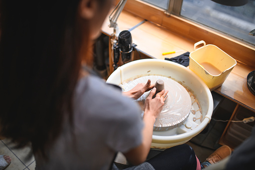 Cropped image of potter molding shape on wheel. Close-up of craftsperson working. She is making clay pot.