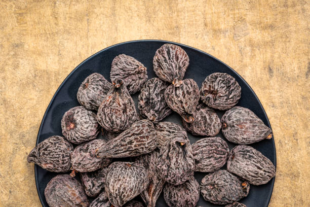 dried mission figs on a black plate against textured bark paper
