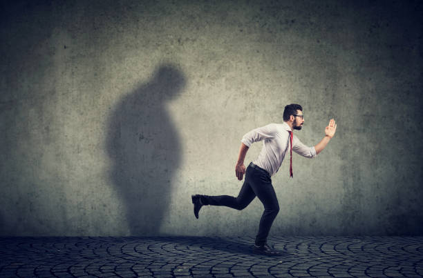 istock Man running away from his sad gloomy fat shadow on the wall. 1136688131