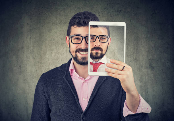 cheerful man holding a tablet with serious self portrait on screen - vanity business business person men imagens e fotografias de stock