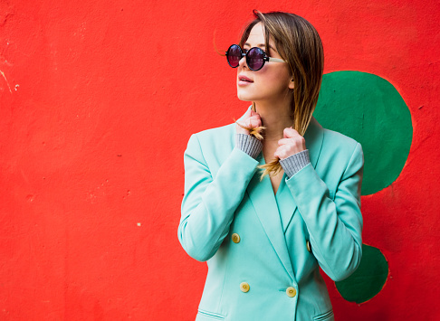 Young woman in Blazer of 90s style and sunglasses in red background.