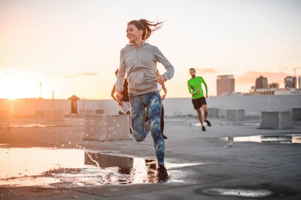 Friends jogging together on terrace against sky Full length of men and woman jogging on rooftop against sky. Young friends are exercising in city. They are in sportswear during sunset. center athlete stock pictures, royalty-free photos & images