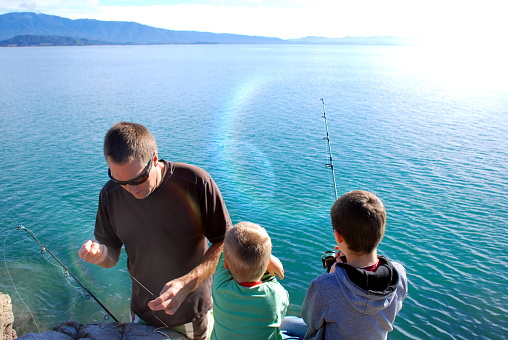 A Father and his Children fishing off the rocks beside the sea .