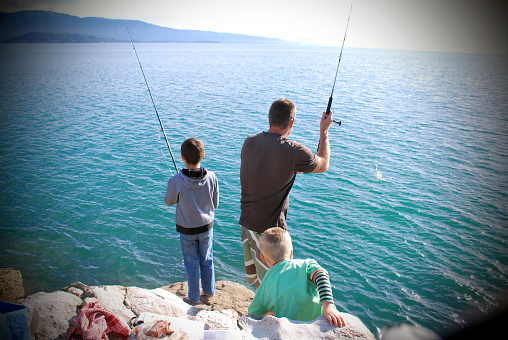 A Father and his Children fishing off the rocks beside the sea .