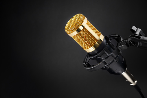 Gold colored condenser microphone other black background. Sound recording equipment.