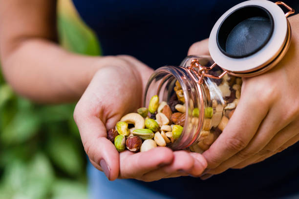 modello bruna che tiene a mano la pentola ermetica di vetro con mix di noci - spuntino foto e immagini stock