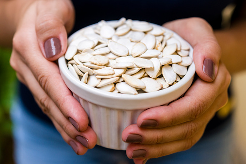 Hand of brunette model holding white pot with pumpkin seeds.