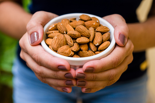 Hand of brunette model holding white pot with natural almonds.