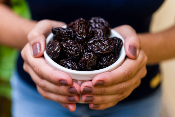 ręka brunetki model trzymającej biały garnek z suszoną śliwką - healthy eating macro close up nut zdjęcia i obrazy z banku zdjęć