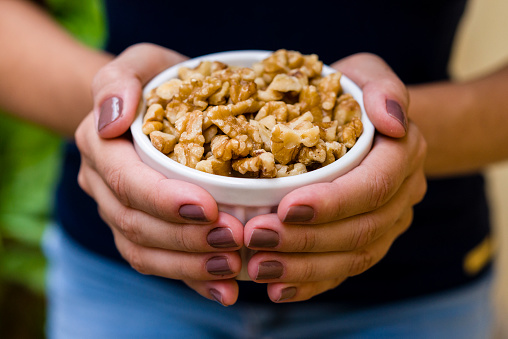 Hand of brunette model holding white pot with pieces of nuts.