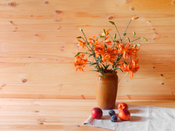 Bouquet of orange lilies in clay vase and fresh fruits near. Wooden background. Bouquet of orange lilies in clay vase and fresh fruits near. Wooden background. View with copy space. red tiger lily stock pictures, royalty-free photos & images