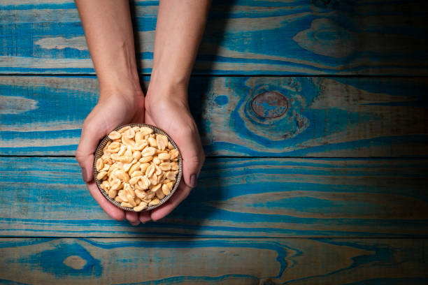 istock Brunette model holding ceramic pot with roasted peanuts on blue wooden background 1136732256