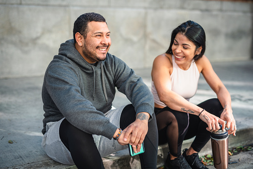 Latin man and woman athlete sitting on the pavement and taking a break