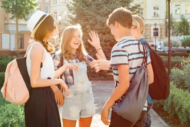Photo of Meeting smiling friends teenagers in the city, happy young people greeting each other, hugging giving high five. Friendship and people concept