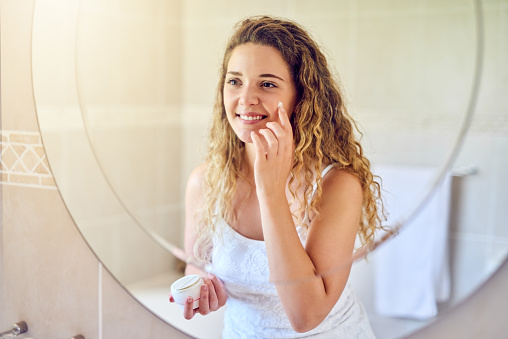 Shot of an attractive young woman applying moisturizer to her face in the bathroom at home
