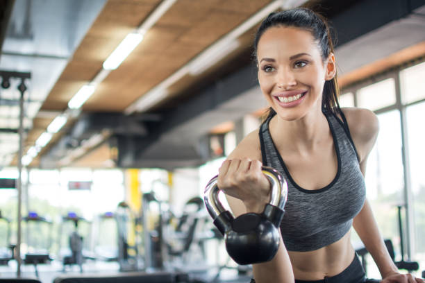 istock Smiling young woman working out with kettle bell in gym 1136774505