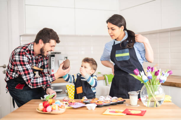Young happy family having fun in the kitchen, Easter Young happy family in the kitchen, father gives a chocolate egg to his son, family having fun in the kitchen muffin tin eggs stock pictures, royalty-free photos & images