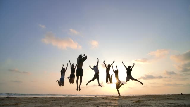 Silhouette of friends jumping on beach during sunset time with happy emotion. 4K resolution. Slow motion shot.