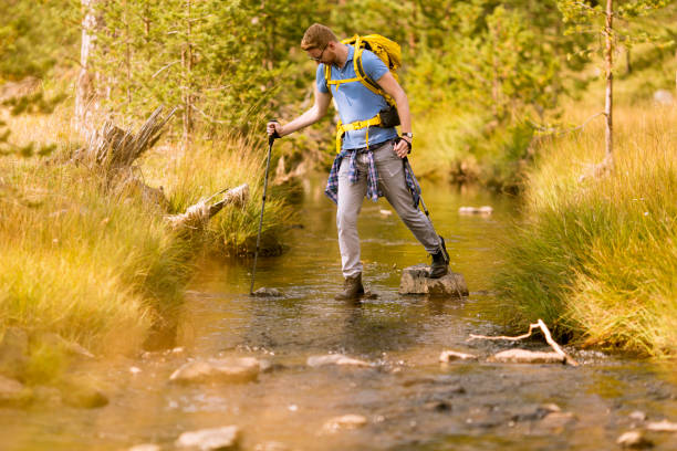 istock Young man crosses a mountain stream on a sunny day 1136778490