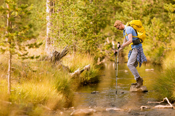 istock Young man crosses a mountain stream on a sunny day 1136778495