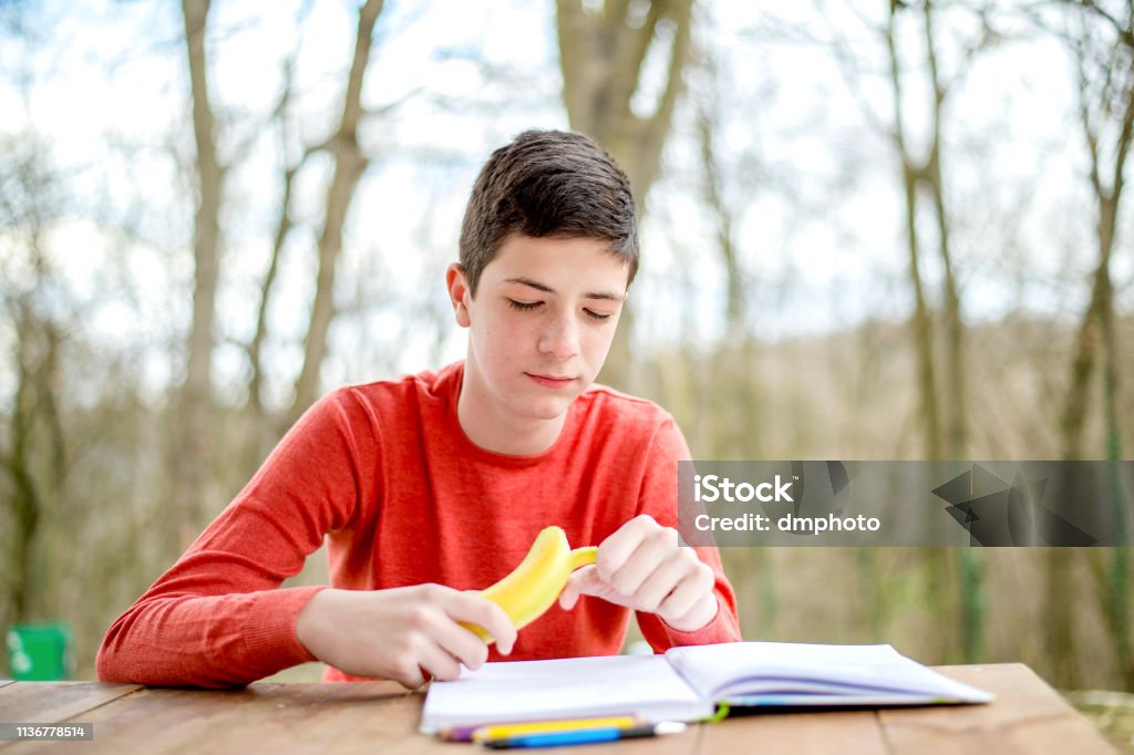 Teenage boy studying in the city park. Time for healthy snack Adolescence Stock Photo