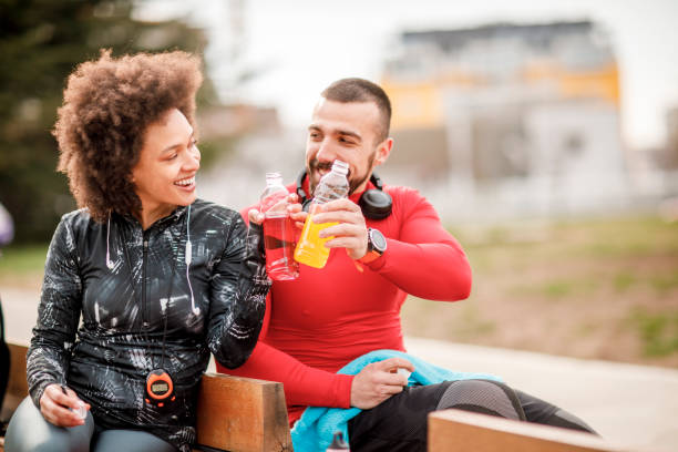 istock Young athletic couple sitting next to each other on a bench in a park and doing a celebratory toast with their energy drinks 1136780363