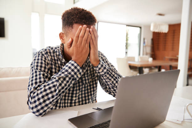 istock Depressed black teenage boy with head in hands using a laptop computer at home, close up 1136780706