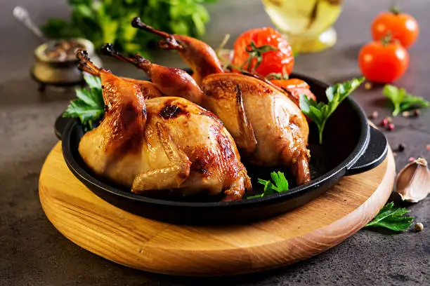 Photo of Baked quails in pan on a dark background