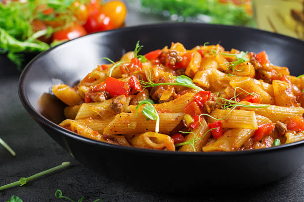 istock Penne pasta in tomato sauce with meat, tomatoes decorated with pea sprouts on a dark table. 1136782273