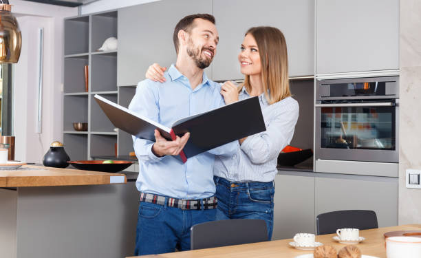 istock Young beautiful couple standing with book in modern kitchen interior 1136783254