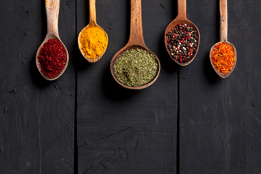 Spices and herbs with old wooden spoons on wooden background