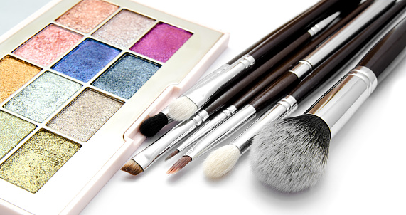 Various set of professional makeup brushes and palette of colourful eye shadows isolated over white background